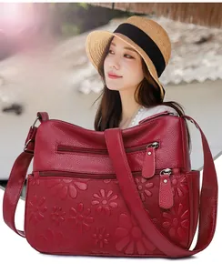 Macro shot of deep red leather bag featuring floral embossing and functional zippers