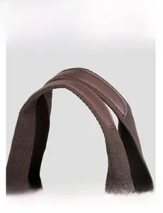 Detail of reinforced leather handle on brown canvas bag with wide woven strap