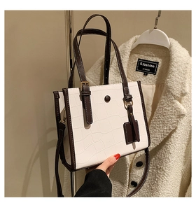 Detail of white crocodile embossed tote bag with brown handles and elegant round clasp