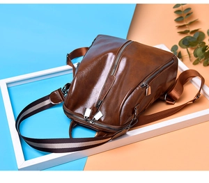 Detail view of brown vintage leather backpack with multi-zipper pockets and striped strap