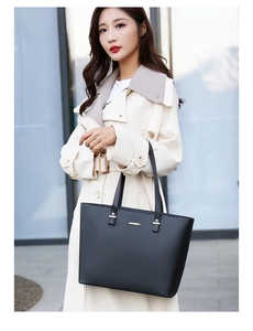 Close-up of minimalist black tote bag with gold metal logo on a beige trench coat