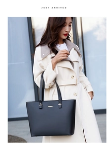 Close-up of black leather tote bag with JINGPIN metal logo on a white trench coat