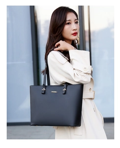Detail of a black leather tote bag with gold logo shown on model for office commute