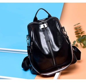 Close-up of black oil wax leather backpack featuring shiny metal zippers and striped strap