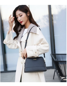 Close-up of black crossbody shell bag with gold JINGSEN logo on a beige trench coat
