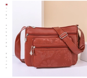 Gros plan d'un sac à bandoulière en cuir PU rouge brique avec gaufrage floral et poches zippées