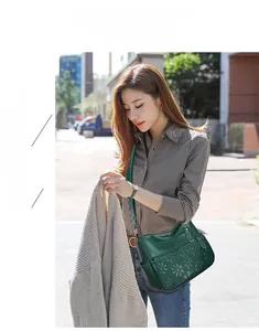 Detail of dark green leather shoulder bag featuring 3D floral embossing and zip pockets