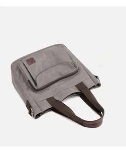 Detail of grey canvas tote bag featuring brown handles and zipped front pocket