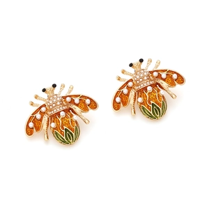 Macro view of gold honey bee earrings with orange enamel and small white pearls