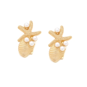 Gros plan de boucles d'oreilles étoile de mer et coquillage dorées ornées de perles blanches