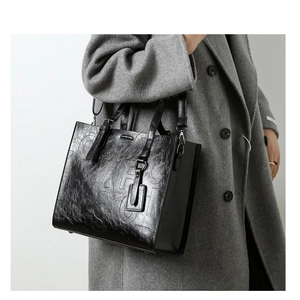 Detail du sac cabas en cuir noir vintage avec lettres embossées porté sur un manteau gris