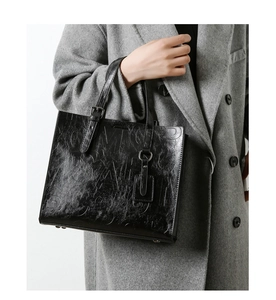 Détail d'un cabas en cuir noir embossé porté par un mannequin en manteau de laine chic