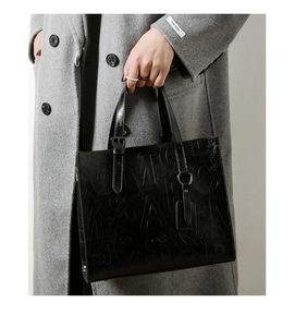 Détail d'un sac cabas noir brillant avec lettres embossées et poignée élégante