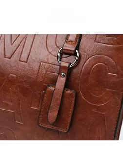 Détail du sac à main en cuir caramel avec lettres gaufrées et finitions métalliques