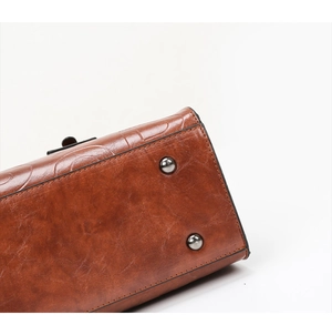 Détail de la base du sac à main en cuir marron avec pieds en métal et coutures