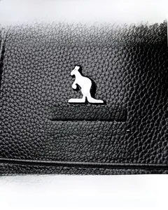 Close-up of black lychee grain leather texture with a silver kangaroo metal logo detail