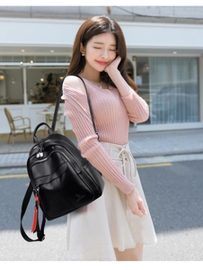 Detail of black lychee leather backpack with red ribbon charm shown on a model
