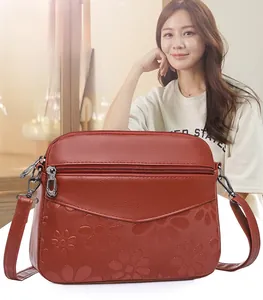 Detail view of reddish-brown crossbody bag with embossed floral texture and triple zippers