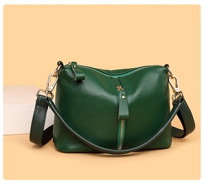 Detail view of dark green pebbled leather handbag with gold zippers and wide strap