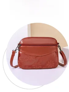 Close-up of brick red pebble leather crossbody bag with embossed floral sunflower pattern