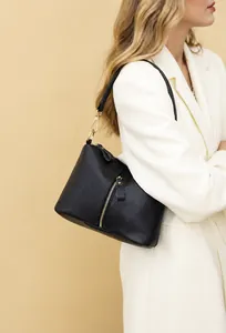 Detail view of black lychee leather handbag with gold zippers and metal clasp on beige background