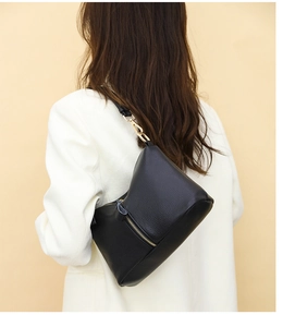 Detail of black pebbled leather crossbody bag with gold hardware worn on a white blazer