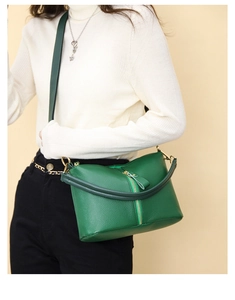 Close-up of dark green textured leather handbag with gold hardware on white sweater