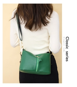 Detail of dark green pebble leather handbag with metal zipper worn by a model