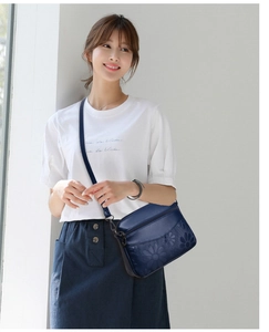 Close-up of deep blue crossbody bag featuring elegant floral embossed patterns and zipper