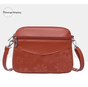 Detail of orange faux leather crossbody bag with daisy embossing and dual zippers