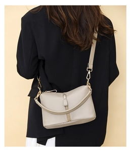 Detail of grey pebbled leather crossbody bag featuring gold hardware and a decorative zipper