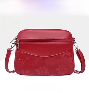 Detail of red faux leather crossbody bag with embossed daisy pattern and front zipper pocket