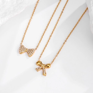 Vue détaillée de deux pendentifs nœud dorés avec incrustation de zircon sur fond de marbre