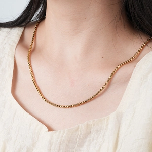 Detailed view of a golden stainless steel box chain necklace worn by a model