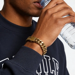 Détail d'un bracelet gourmette doré avec fermoir pliable carré porté au poignet masculin