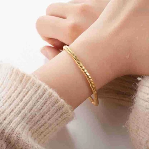 Détail d'un élégant bracelet chaîne maille serpent dorée porté sur une manche en maille