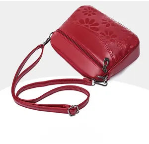 Close-up of red embossed crossbody bag featuring floral daisy patterns and metal hardware