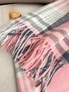 Detailed view of pink and grey plaid scarf texture with soft tassels on warm beige background
