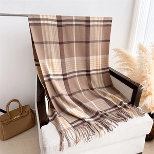 Detail of soft earth tone plaid scarf with fringe tassels on a cozy armchair