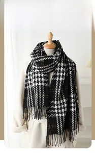 Close-up of black and white houndstooth scarf with brown lines and tassels on a cream coat