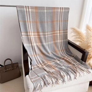 Detail of plaid scarf with tassels on white chair featuring soft cashmere-like texture