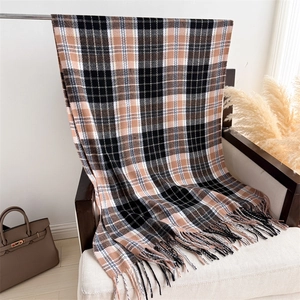 Macro detail of brown and black plaid scarf with fringe on a white textured sofa