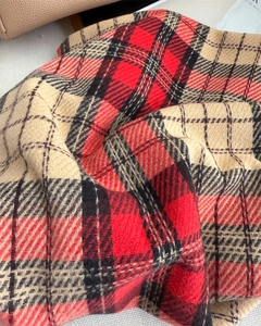 Detailed macro view of the thick twill texture on a warm plaid scarf with tassels