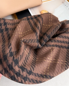 Detail of brown houndstooth scarf with golden embroidery and elegant tassel edges