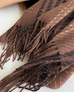 Detailed close-up of herringbone weave scarf with gold threads and tassel trim