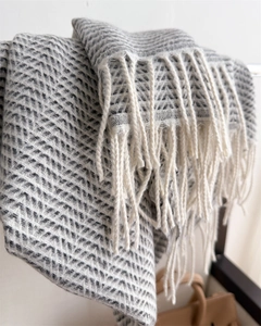 Close-up of grey herringbone knit pattern and white fringe tassels on warm winter scarf