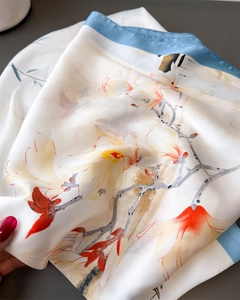 Dettaglio di un foulard in seta con stampa di magnolia e bordo blu su fondo grigio