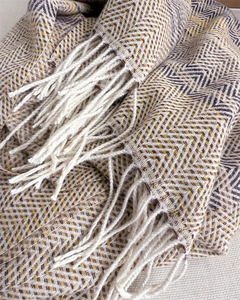 Detailed view of yellow and purple herringbone knit scarf featuring thick white fringe tassels