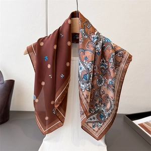 Elegant paisley and floral silk square scarf displayed on a wooden hanger with a model