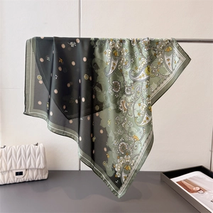 Elegant green paisley print silk scarf displayed with a stylish handbag and magazine